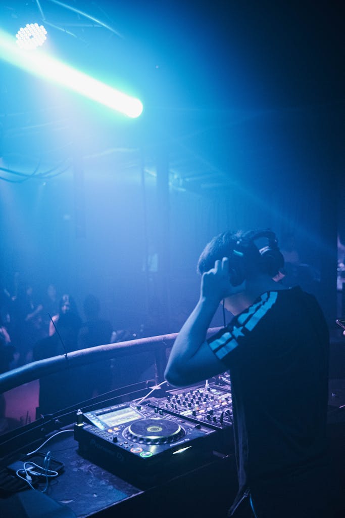 DJ at mixing console in vibrant nightclub with illuminated atmosphere and energetic crowd.